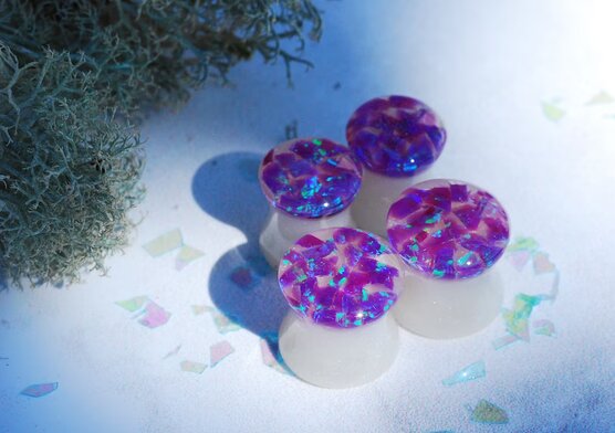 four purple opal ear gauges side by side
