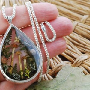 hand holding microhabitat necklace with forest landscape