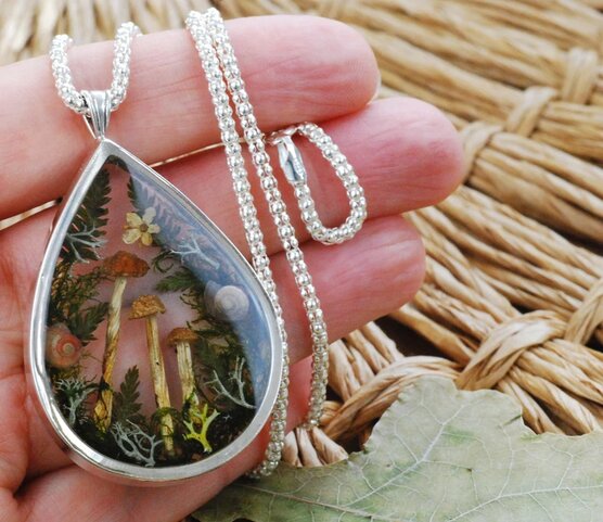 hand holding microhabitat necklace with forest landscape