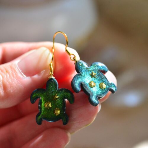 Hand holding pair of green turtle earrings